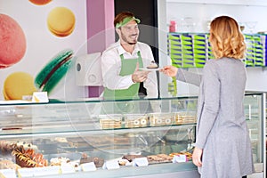 Seller in confectionery gives cup cake to customer