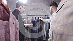 Seller in the costume shop helps the young man to choose a suit
