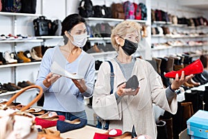 Seller in face mask helping old woman to choose new shoes