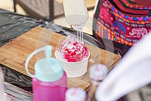 The seller is pouring sweetened condensed milk over the shaved ice