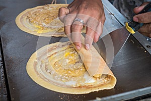 Seller rolling Khanom Tokyo thin flat pancake Thai street snack