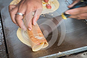 Seller rolling Khanom Tokyo thin flat pancake Thai street snack