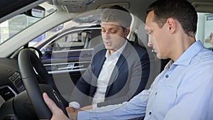 Seller sitting inside car with buyer, shows customer man new