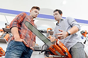 The seller in the store shows the customers a chainsaw.