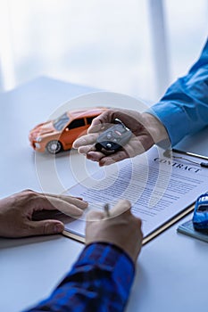 Selling a car. Management concept. The dealer gives the car keys to the new owner or renter with a contract of insurance.