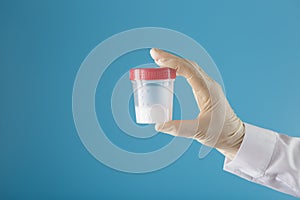 Semen in a jar for analysis in the doctor`s hand on a blue background