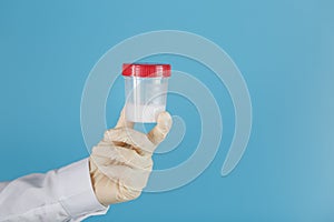 Semen in a jar for analysis in the doctor`s hand on a blue background
