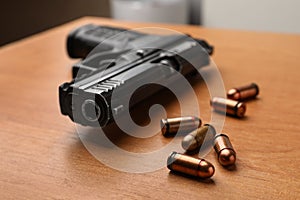Semi-automatic pistol and bullets on wooden table indoors, closeup