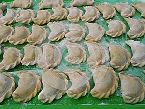Semi-finished dumplings on a green kitchen tray with flour