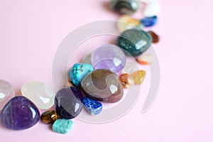 Semi-precious stones of different colors on a pink background. Amethyst, rose quartz, agate, apatite, aventurine, olivine,