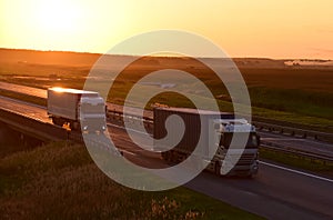 Semi-trailer truck by driving along highway on sunset background. Goods delivery by roads. Services and Transport logistics.