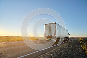 Semi-truck with cargo trailer driving on highway hauling goods in evening. Delivery transportation and logistics concept