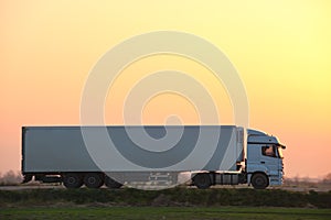 Semi-truck with cargo trailer driving on highway hauling goods in evening. Delivery transportation and logistics concept