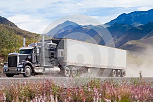 Semi truck on dusty road in mountain landscape