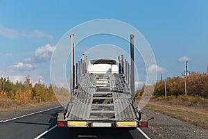 Semi truck with empty car carrier trailer running on the road in sunny autumn day.back view.car transporter.transport concept,work