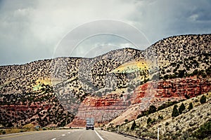 Semi truck on highway through badlands of Utah withcolorful  red rock cliffs and chalk mountains