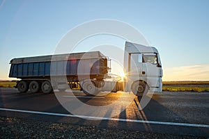 Semi-truck with tipping cargo trailer transporting sand from quarry driving on highway hauling goods in evening