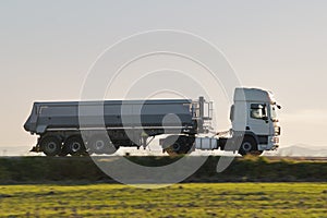 Semi-truck with tipping cargo trailer transporting sand from quarry driving on highway hauling goods in evening