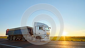 Semi-truck with tipping cargo trailer transporting sand from quarry driving on highway hauling goods in evening