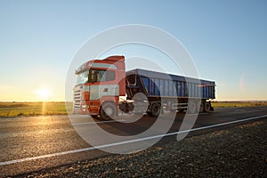 Semi-truck with tipping cargo trailer transporting sand from quarry driving on highway hauling goods in evening