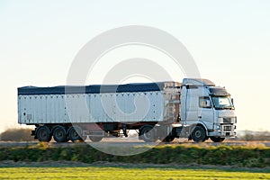 Semi-truck with tipping cargo trailer transporting sand from quarry driving on highway hauling goods in evening