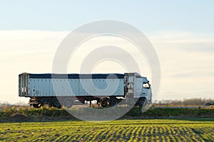 Semi-truck with tipping cargo trailer transporting sand from quarry driving on highway hauling goods in evening