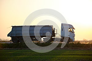 Semi-truck with tipping cargo trailer transporting sand from quarry driving on highway hauling goods in evening