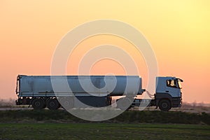 Semi-truck with tipping cargo trailer transporting sand from quarry driving on highway hauling goods in evening