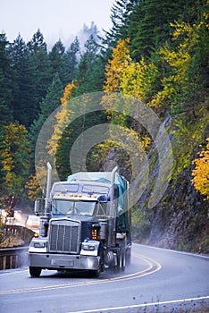 Semi truck trailer with cargo on winding autumn reoad in rain