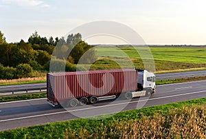 Semi truck transporting sea container on highway on sunset background. Shipping Containers Delivery, Maritime Services and