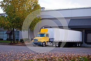 Semi Truck yellow cab and trailer parked at dock for unloading