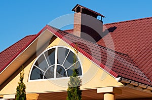 Semicircle window and brick chimney on the red metal tile roof, house exterior