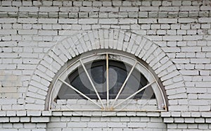 Semicircular barred window in a white brick wall