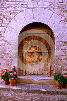 Semicircular entrance to the stone house, wooden antique door, flowers in pots.