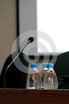 Seminar podium with blank screen, microphone and bottles of water on table ready for the speaker