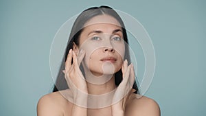 A seminude woman touches her clean and smooth face with wellgroomed fingers. Close up portrait of young woman isolated