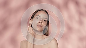 Seminude woman uses a makeup brush in the studio on a pink background close up. A woman does contouring, applies powder