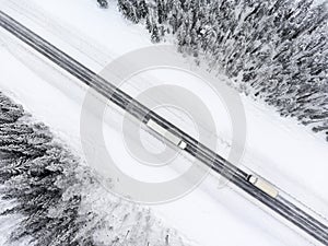Semitrailer truck and lorry driving from the opposite direction on slippery winter asphalt highway, top view from drone