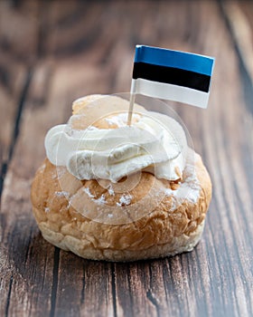 Semla, fastelavnsbolle, fastlagsbulle. Decorated with an Estonian flag. On a wooden table with a dark background.