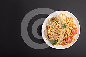 Semolina pasta with tomato pesto sauce, orange and herbs on a black background. Top view, copy space