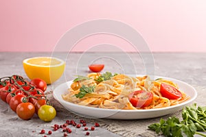 Semolina pasta with tomato pesto sauce, orange and herbs on a gray and pink background. Side view, selective focus, copy space