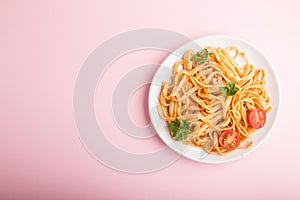 Semolina pasta with tomato pesto sauce, orange and herbs on a pink pastel background. Top view, copy space