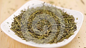 Sencha green tea dry leaves falling into a white saucer