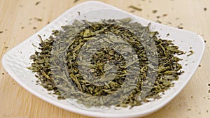 Sencha green tea dry leaves in a white saucer