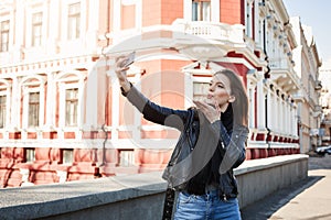 Sending warm kiss to my followers. City shot of young charming woman holding smartphone, taking selfie while being