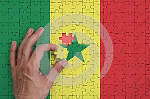 Senegal flag is depicted on a puzzle, which the man`s hand completes to fold