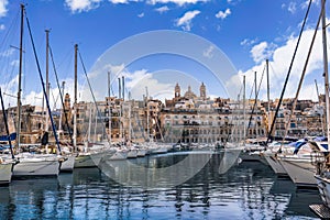 Senglea, Malta waterfront with moored leisure boats and traditional limestone buildings with balconies against blue sky with