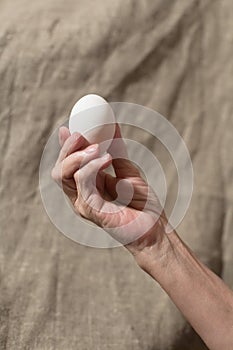 Senile hand holds a white chicken egg