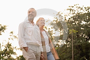 Senior active caucasian couple holding hands looks happy and carefree in the park in the afternoon autumn sunlight with copy space