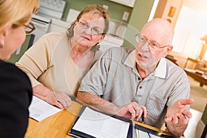 Sweet Senior Adult Couple Going Over Documents in Their Home with Agent At Signing